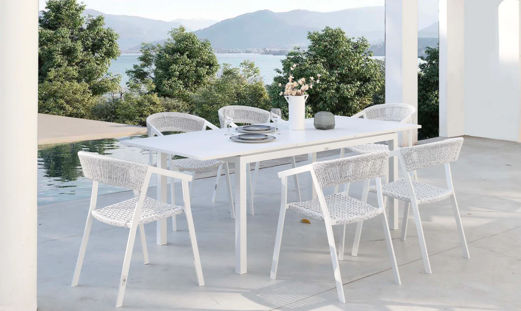 White extendable outdoor dining table with white outdoor dining chairs in a poolside setting