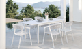 White extendable outdoor dining table with white outdoor dining chairs in a poolside setting