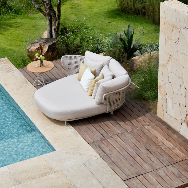ALMA round outdoor daybed beside a pool in a landscaped garden