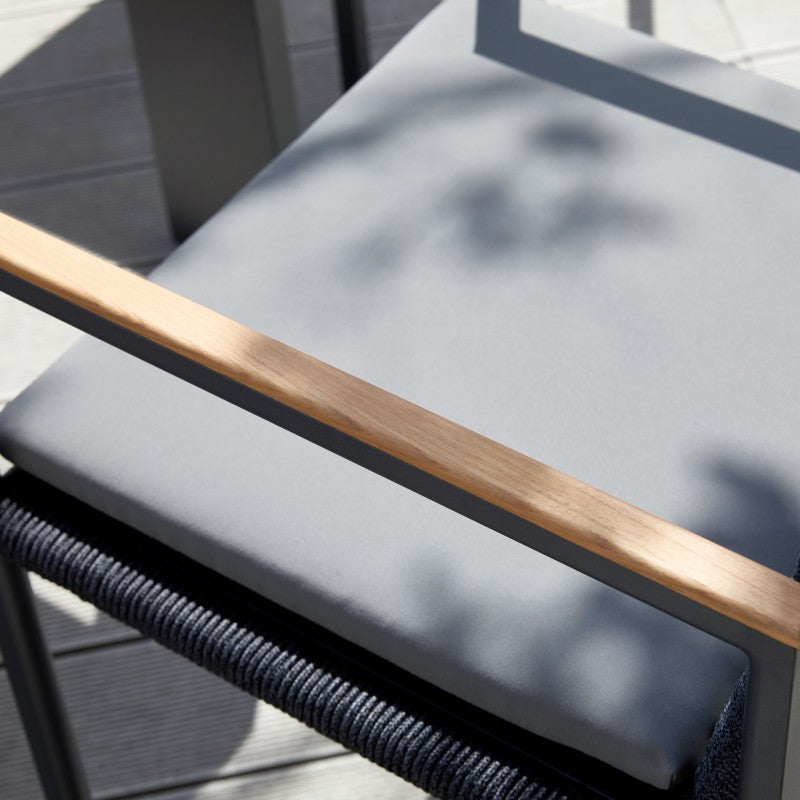 Detail of the grey cushion and teak arm on the SUNRISE outdoor dining armchair